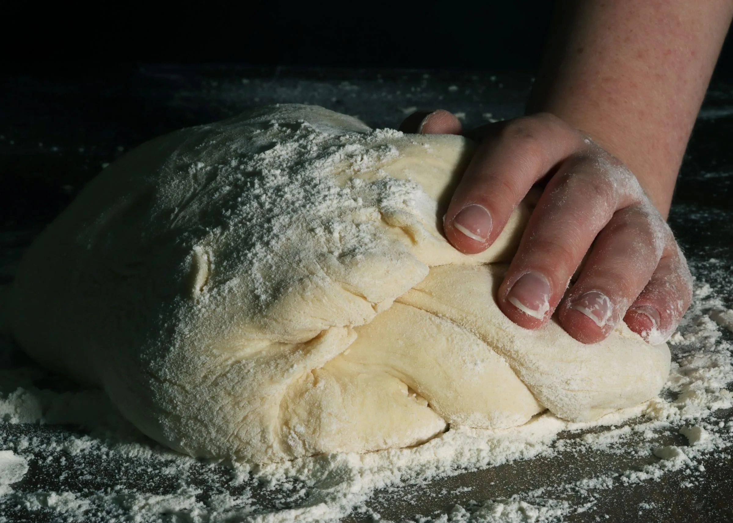 Mains d’un boulanger façonnant une pâte à pain sur un plan de travail fariné